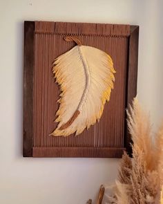 a wooden frame with a painting of a yellow leaf on it and some dried plants