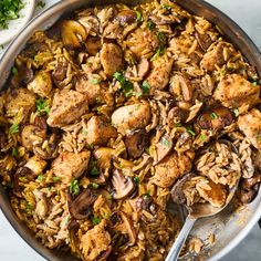 a skillet filled with chicken and rice covered in mushrooms, parsleys and garnishes