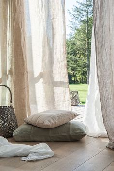 a window with sheer curtains and pillows on the floor