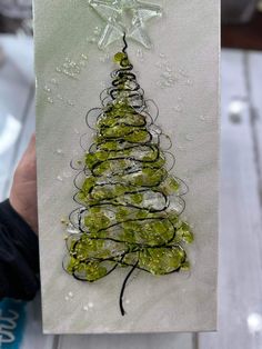 a hand holding up a card with a christmas tree made out of green glass beads