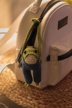 a crocheted stuffed animal hanging from the side of a white bag on top of a table