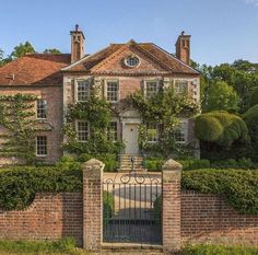 a large brick house with an iron gate and ivy covered hedges surrounding the front entrance