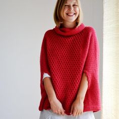 a woman wearing a red knitted ponchy with white trims and smiling