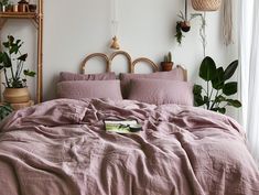 an unmade bed with pink linens and potted plants on the wall behind it