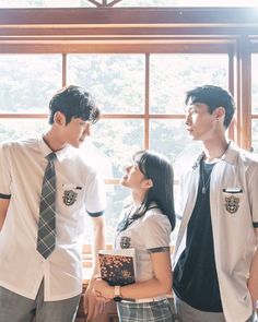 three young people standing next to each other in front of a window with trees outside