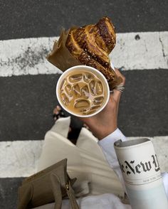 a person holding up a cup of coffee and some food in front of their face