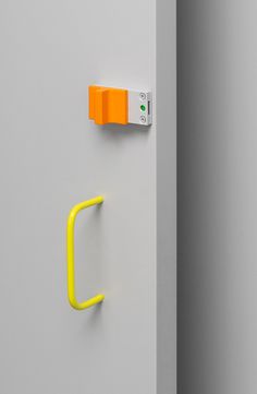 an orange handle on the side of a gray wall next to a yellow hook and white door