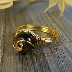 "Golden Tigers Eye Gemstone and Sterling Silver, Yellow or Rose Gold Filled Wire Wrapped Swirl Ring; Custom Made to Size ❀ This round golden tigers eye gemstone bead and wire wrapped ring is handmade with an approximately 8mm by 5mm bead and your choice of wire for the band. ❀ This ring (as well as all the others in my shop) is custom made to any size from 4 to 14 including half and quarter sizes! ❀ This ring can be made in Sterling Silver Filled Wire, Argentium Sterling Silver wire (tarnish res Wire Wrapped Rose Gold Rings, Adjustable Spiral Wire Wrapped Jewelry, Handmade Adjustable Swirl Jewelry, Gold Wire Wrapped Swirl Jewelry, Gold Swirl Wire Wrapped Jewelry, Brown Spiral Jewelry As A Gift, Wire Wrapped Swirl Jewelry As Gift, Adjustable Swirl Jewelry For Gifts, Adjustable Nickel-free Swirl Jewelry