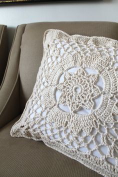 a white crocheted pillow sitting on top of a couch next to a painting