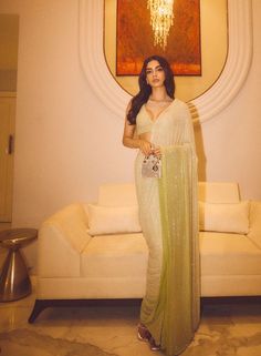 a woman standing in front of a couch wearing a green sari and holding a purse