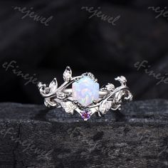 a white opal ring with leaves and vines around it on top of a piece of wood