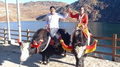 two people riding on the backs of donkeys in front of a body of water