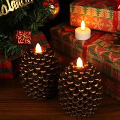 two pine cone candles sitting next to presents under a christmas tree