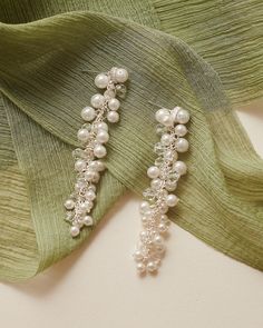 a pair of earrings with pearls hanging from it's side on a green scarf