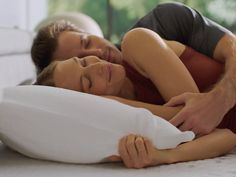 a man and woman laying in bed with pillows on the floor next to each other