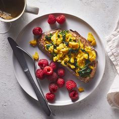 a white plate topped with toast and raspberries next to a cup of coffee