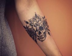 a woman's arm with a skull and flowers tattoo on the left inner forearm