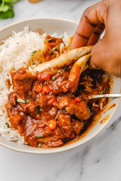 someone is holding a fork in a bowl filled with rice and meat curry on the side