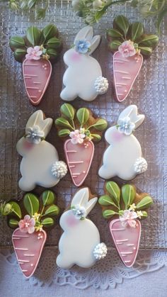 some decorated cookies are sitting on a table with green leaves and pink flowers in the shape of bunnies