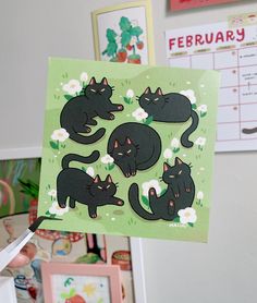 a person holding up a card with black cats on it and flowers in the background