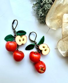 two red apples and one green apple are hanging from the back of ear hooks on a white surface