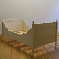 a white bed frame with scalloped edges on a wooden floor next to a wall