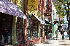 people are walking down the sidewalk in front of shops and businesses on a sunny day