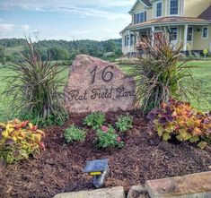 a large rock sitting in the middle of a flower bed next to a house and yard