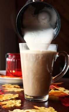 a cup filled with white liquid sitting on top of a table next to autumn leaves