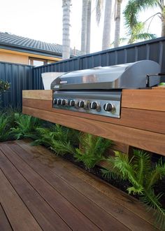 an outdoor grill on a wooden deck surrounded by greenery and palm tree's