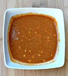 a white bowl filled with chili sauce on top of a wooden table next to a spoon