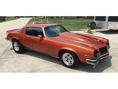 an orange muscle car parked in front of a trailer