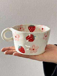 a hand holding a white cup with strawberries on it and flowers painted on the inside