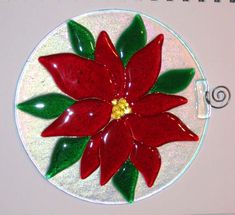 a red flower with green leaves is on a white circle ornament that hangs from a spiral wire