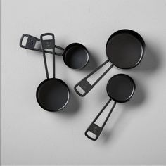 four black pans and spatulas sitting on top of a white table next to each other