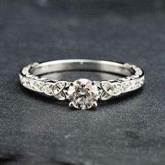 a white gold engagement ring with an intricate design on the side and a round diamond in the center