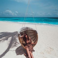 a woman sitting in a hammock on the beach with an umbrella over her head