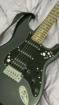 a black electric guitar laying on top of a white bed sheet with its neck and bridge missing