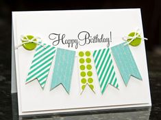 a happy birthday card with green and blue ribbons on it's edge, sitting on a table