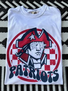 Get this popular new Patriots Mascot shirt and show off your school spirit in style!  Each shirt is printed in-house by me using high-quality materials on a Comfort Colors shirt, known for its exceptional comfort, style, and durability. Shown in Natural. Even the glitter is printed! No need to worry about peeling glitter vinyl, or messy glitter flakes. Available in unisex sizes S to 3X, and youth sizes, we've got you covered regardless of your preferred fit. The Preppy Patriots Shirt features a classic crew neck and short sleeves, making it suitable for year-round wear. The flattering silhouette ensures a comfortable and stylish fit for both men and women. Please note that ivory is ONLY available in Adult sizes!  Note: As each shirt is individually printed, slight variations in color and p Cheap White School Spirit Shirt, Sports Fan Cotton Shirt For Fan Merchandise, Cotton Fan Apparel Shirt For Game Day, White Graphic Tee Shirt For Fan Gear, Sports Fan Cotton Shirt, White Graphic Tee For Fan Gear, White Graphic Print Shirt For Fans, White Team Spirit Shirt For Fans, White Shirt With Team Spirit For Fans