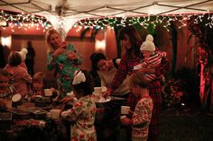 a group of people standing around a table covered in food and drinks with christmas lights on the wall behind them