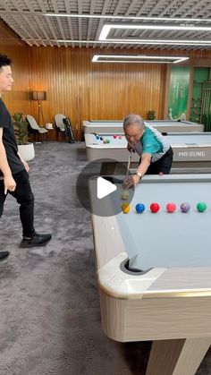 two men are playing pool in an indoor bowling alley with balls on the table and one man is bending over