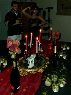 a table topped with lots of candles and vases filled with flowers next to wine bottles