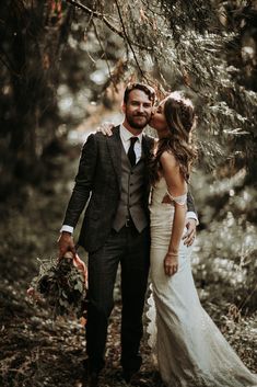 a bride and groom kissing in the woods