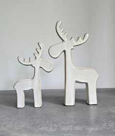 two white ceramic deer figurines sitting next to each other on a gray surface