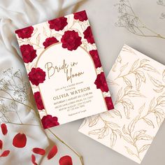 two wedding cards with red flowers and gold foil on them, sitting next to each other