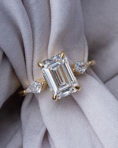 an emerald cut diamond sits on top of a white cloth with three diamonds around it