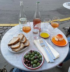 a table topped with plates of food and glasses of wine on top of a white table