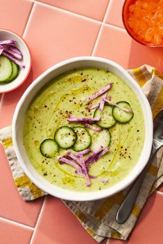 a bowl of soup with cucumbers and red onion on the side next to a spoon