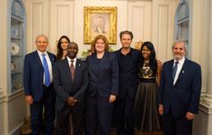 a group of people in suits and ties posing for a photo with a portrait on the wall behind them